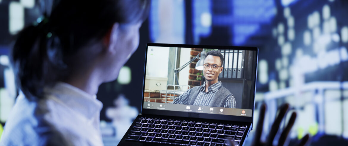 Asian man in videocall with coworker while strolling around city streets at night, giving him work updates. Person using laptop to show colleague surroundings in nighttime urban environment