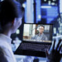 Asian man in videocall with coworker while strolling around city streets at night, giving him work updates. Person using laptop to show colleague surroundings in nighttime urban environment